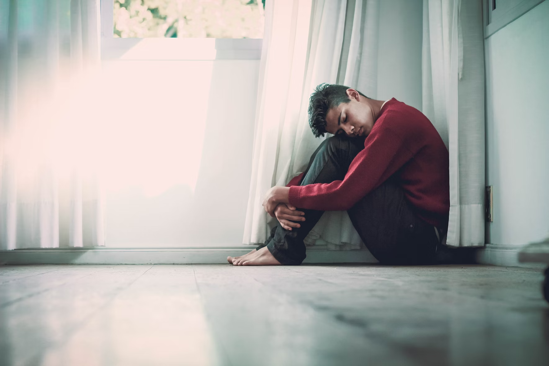 A depressed-looking teen boy sits on the floor.
